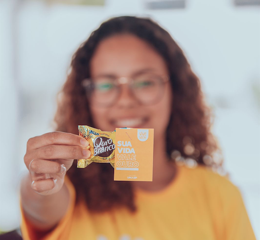 Uma jovem segura o cartão e um bombom ouro branco.