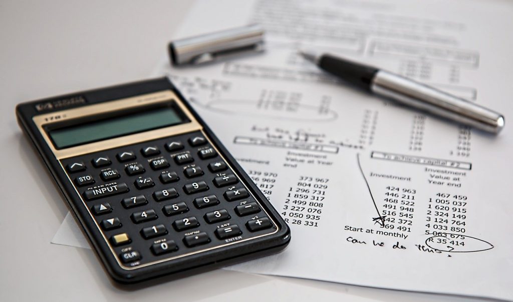Calculadora, caneta e papel com dados contábeis.